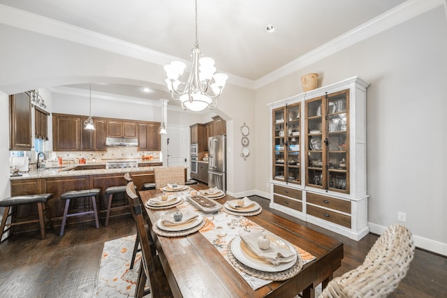 dining area with sink, crown molding, dark wood-type flooring, and a chandelier