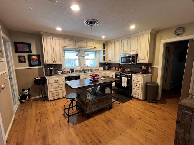 kitchen featuring a kitchen bar, sink, a textured ceiling, light hardwood / wood-style floors, and black appliances