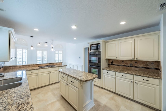 kitchen with visible vents, wainscoting, a center island, black appliances, and pendant lighting