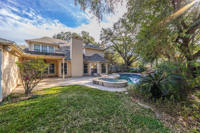 back of property featuring a chimney, fence, a yard, a patio area, and a pool with connected hot tub