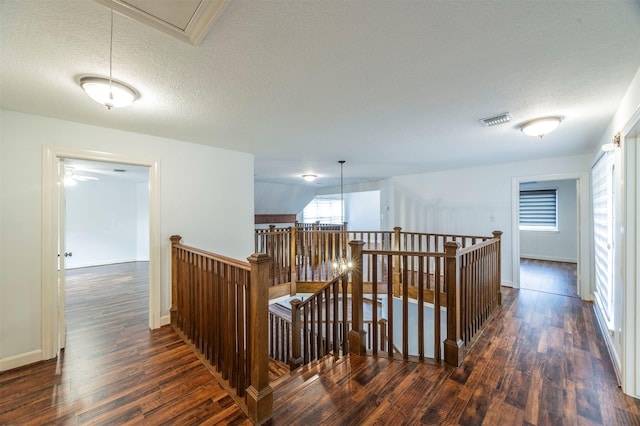 hallway with a textured ceiling, dark wood-style flooring, visible vents, an upstairs landing, and attic access