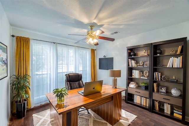 home office with a ceiling fan, visible vents, and dark wood finished floors