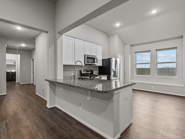 kitchen featuring appliances with stainless steel finishes, white cabinetry, backsplash, a kitchen breakfast bar, and kitchen peninsula