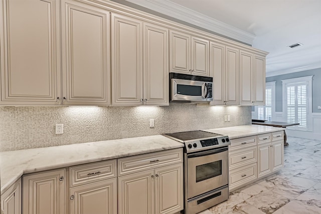 kitchen with tasteful backsplash, ornamental molding, stainless steel appliances, light stone countertops, and cream cabinets