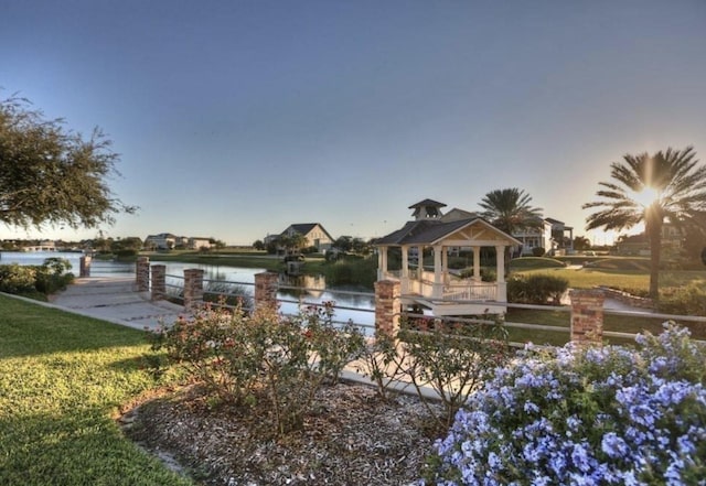 back house at dusk with a water view, a gazebo, and a lawn