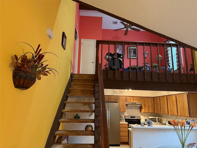 staircase with vaulted ceiling, a textured ceiling, and ceiling fan