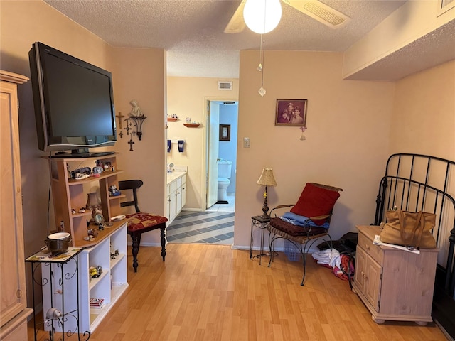 living area with ceiling fan, a textured ceiling, and light wood-type flooring