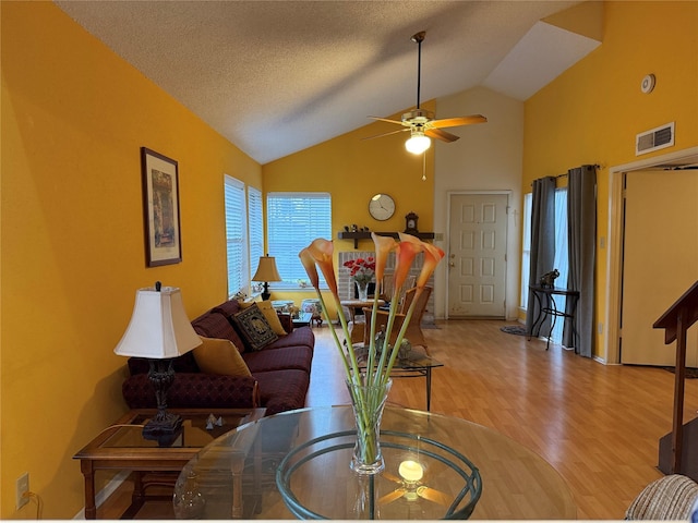 living room featuring ceiling fan, lofted ceiling, a textured ceiling, and light wood-type flooring