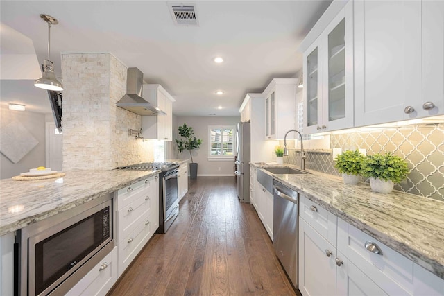 kitchen featuring hanging light fixtures, stainless steel appliances, white cabinets, and wall chimney exhaust hood