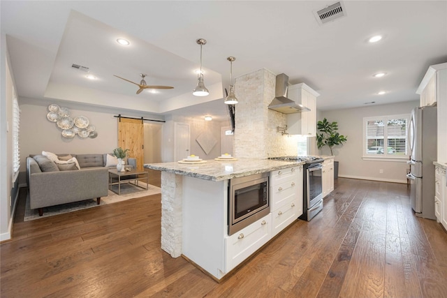 kitchen with white cabinetry, a barn door, wall chimney exhaust hood, and appliances with stainless steel finishes