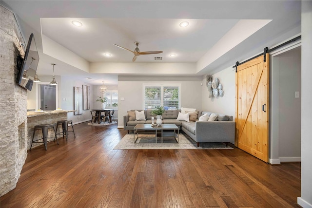 living room featuring a barn door, dark hardwood / wood-style floors, ceiling fan, and a tray ceiling