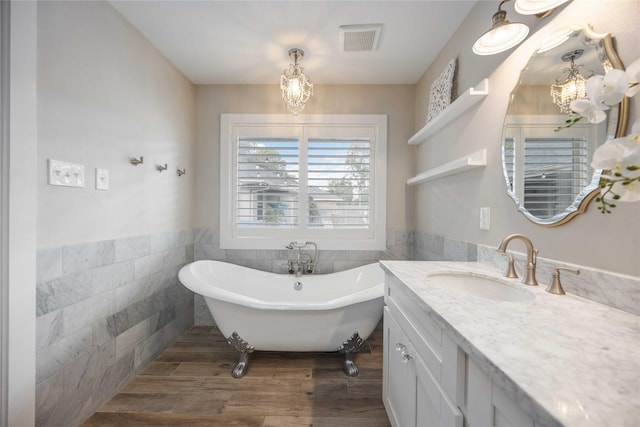 bathroom featuring a washtub, tile walls, vanity, wood-type flooring, and a chandelier