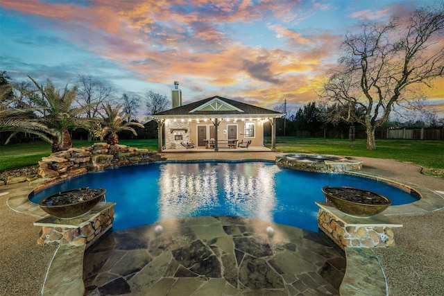 pool at dusk featuring an outbuilding, an in ground hot tub, and a patio area