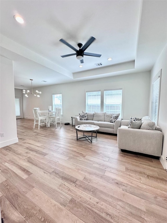 living room with a tray ceiling, ceiling fan with notable chandelier, and light hardwood / wood-style floors