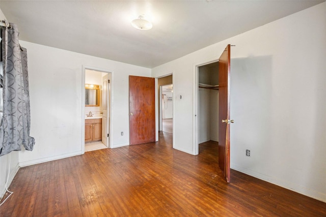 unfurnished bedroom with ensuite bathroom, dark wood-type flooring, and a closet