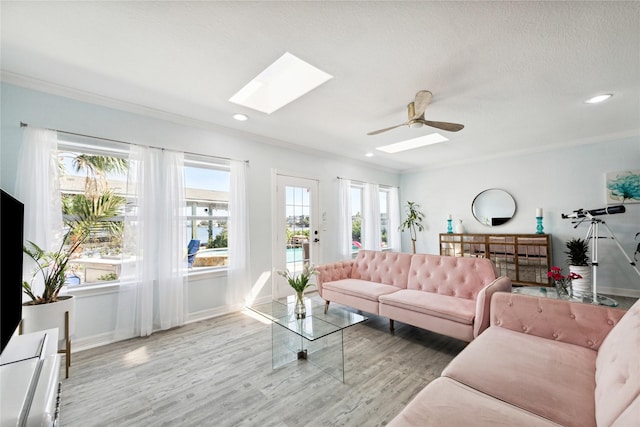 living room with a skylight, ceiling fan, light hardwood / wood-style floors, crown molding, and a textured ceiling