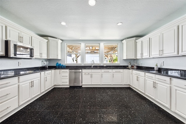 kitchen featuring stainless steel appliances, white cabinetry, sink, and dark stone counters