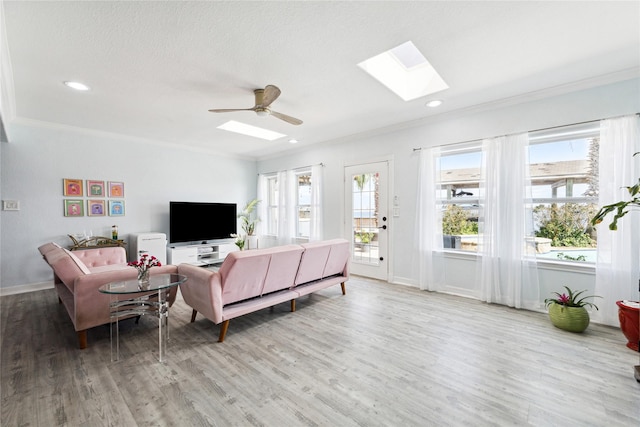 living room featuring ceiling fan, ornamental molding, a skylight, and light hardwood / wood-style flooring