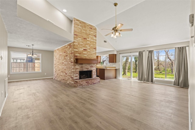 unfurnished living room featuring baseboards, light wood-style flooring, a textured ceiling, a brick fireplace, and ceiling fan with notable chandelier