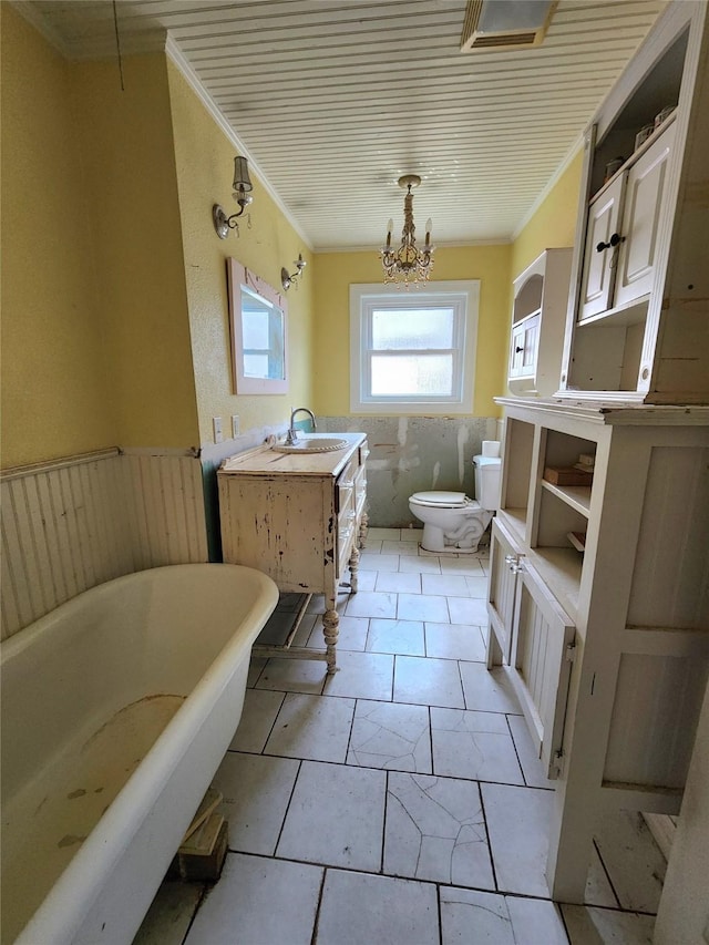 bathroom featuring a notable chandelier, vanity, a tub to relax in, toilet, and ornamental molding