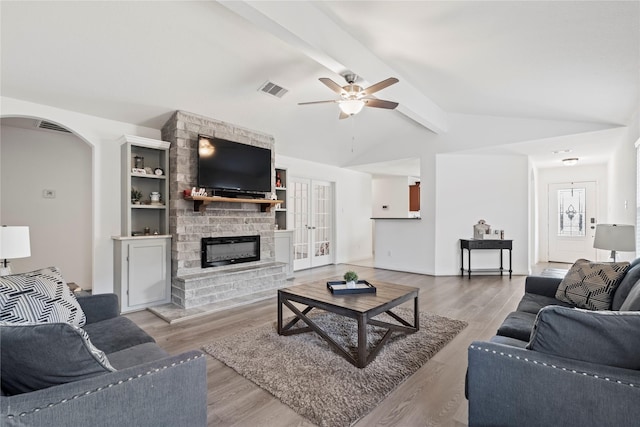 living room featuring french doors, lofted ceiling with beams, ceiling fan, a fireplace, and light hardwood / wood-style floors