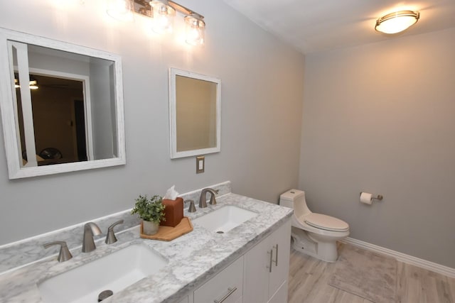 bathroom featuring toilet, double vanity, baseboards, and a sink