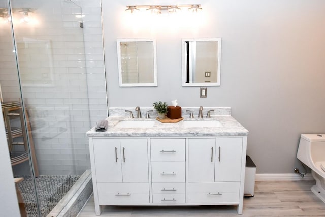 bathroom with double vanity, a shower stall, a sink, and wood finished floors