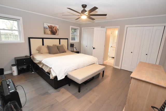 bedroom with baseboards, ceiling fan, ornamental molding, wood finished floors, and two closets