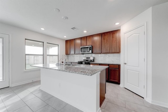 kitchen with sink, light stone counters, stainless steel appliances, a kitchen island with sink, and decorative backsplash