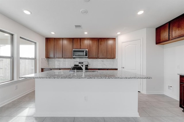 kitchen featuring light stone countertops, appliances with stainless steel finishes, sink, and a center island with sink