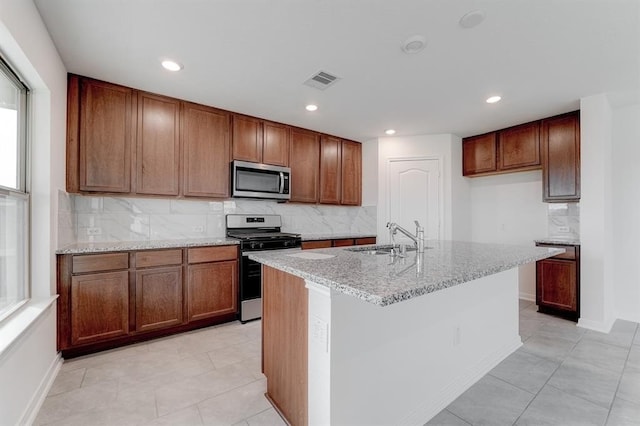 kitchen featuring an island with sink, sink, decorative backsplash, stainless steel appliances, and light stone countertops