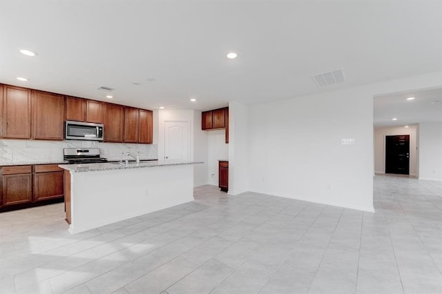 kitchen with sink, appliances with stainless steel finishes, tasteful backsplash, light stone countertops, and an island with sink