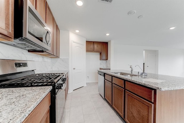 kitchen featuring sink, appliances with stainless steel finishes, light stone countertops, a center island with sink, and decorative backsplash