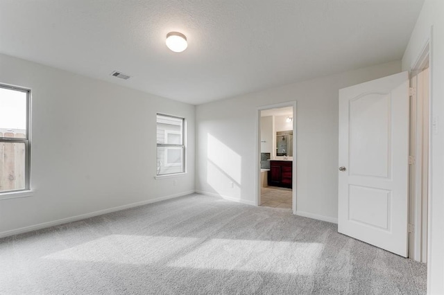 unfurnished bedroom with multiple windows, connected bathroom, light colored carpet, and a textured ceiling