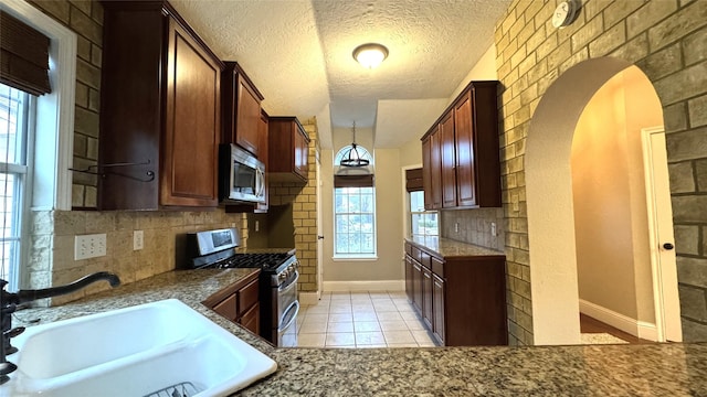 kitchen featuring sink, a textured ceiling, light tile patterned floors, stainless steel appliances, and backsplash