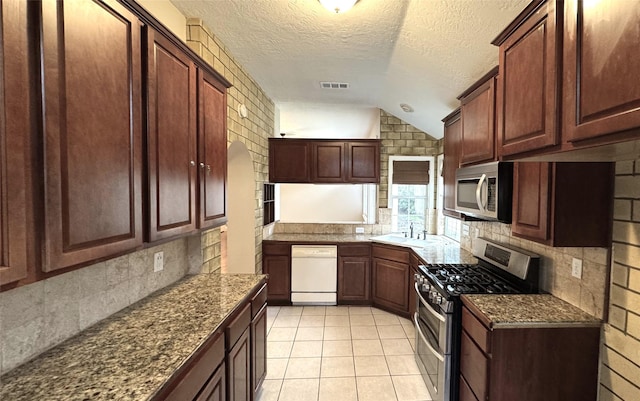 kitchen with dark stone countertops, stainless steel appliances, tasteful backsplash, light tile patterned flooring, and vaulted ceiling