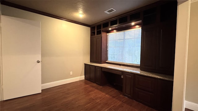 unfurnished office featuring dark wood-type flooring, ornamental molding, and built in desk