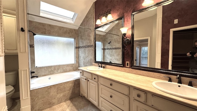 bathroom with lofted ceiling with skylight, vanity, tiled bath, tile patterned floors, and toilet