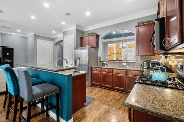 kitchen featuring light hardwood / wood-style flooring, a breakfast bar area, stainless steel refrigerator with ice dispenser, an island with sink, and range with gas cooktop