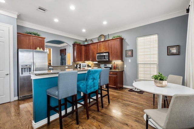 kitchen with a kitchen bar, crown molding, dark hardwood / wood-style flooring, stainless steel appliances, and decorative backsplash