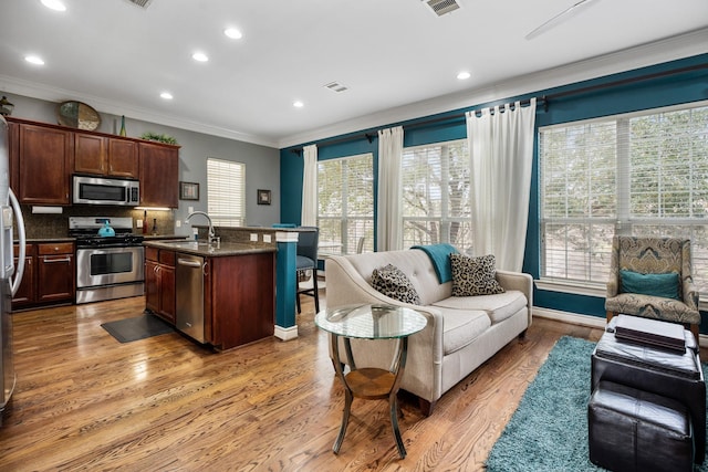 kitchen with crown molding, appliances with stainless steel finishes, sink, and an island with sink