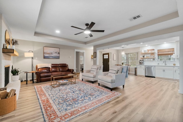 living room with a raised ceiling, sink, a fireplace, and light hardwood / wood-style floors