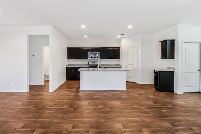 kitchen with stainless steel appliances, light stone countertops, a kitchen island with sink, and dark hardwood / wood-style floors