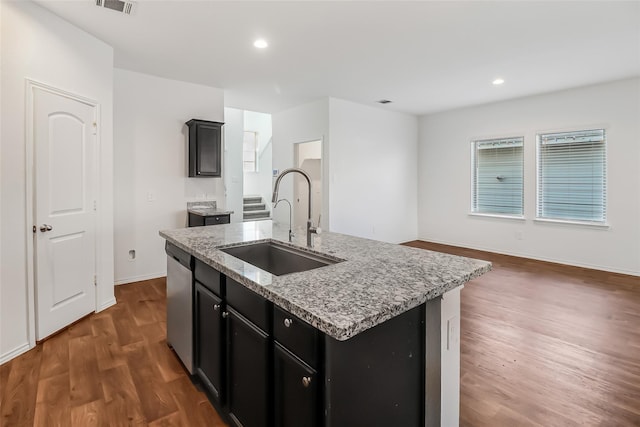 kitchen featuring sink, a kitchen island with sink, dark hardwood / wood-style floors, light stone counters, and stainless steel dishwasher