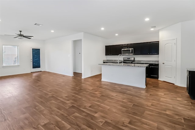 kitchen featuring sink, light stone counters, a center island with sink, dark hardwood / wood-style flooring, and stainless steel appliances