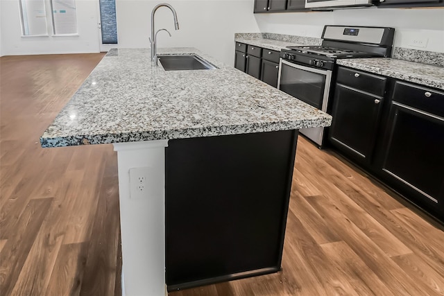 kitchen with sink, gas range, a kitchen island with sink, light stone countertops, and light hardwood / wood-style floors