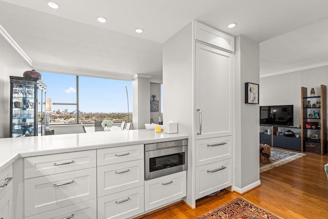 kitchen featuring white cabinetry, stainless steel microwave, crown molding, and light wood-type flooring