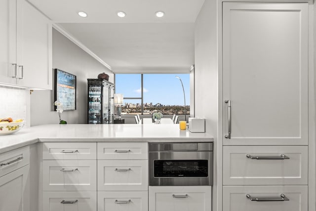 kitchen with backsplash, ornamental molding, stainless steel oven, and white cabinets