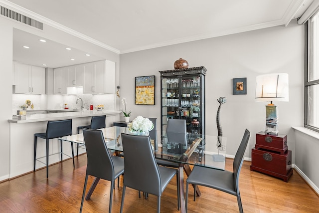 dining room with ornamental molding, light hardwood / wood-style floors, and sink