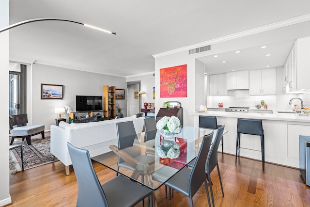 dining space with sink, wood-type flooring, and ornamental molding